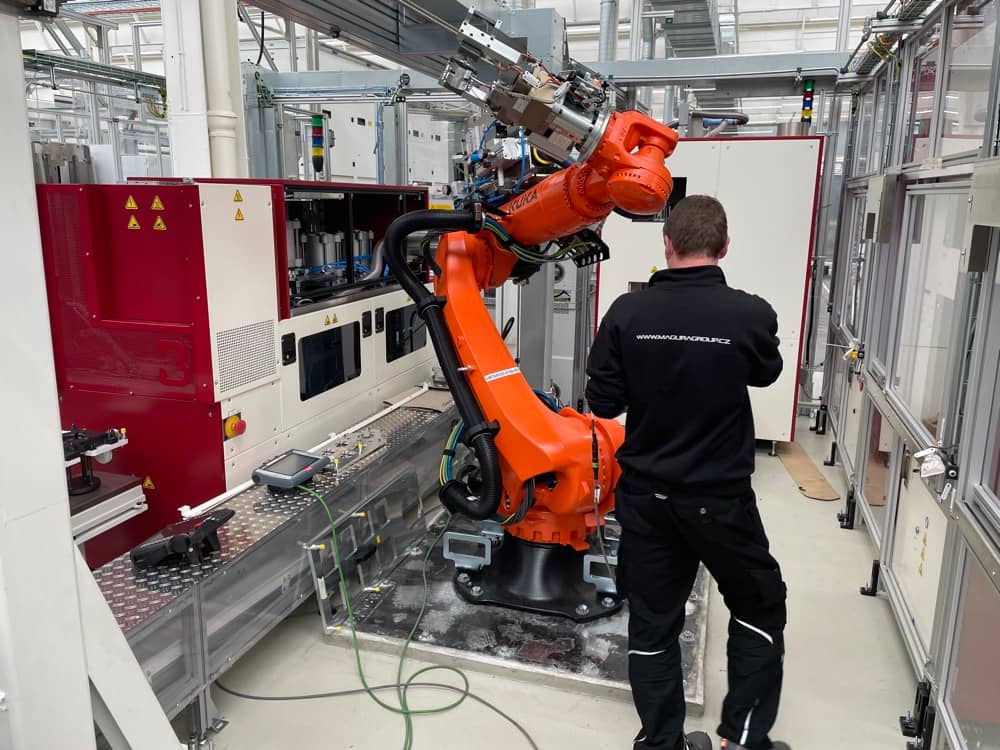 Programování oranžového robotického ramene technikem v hale.