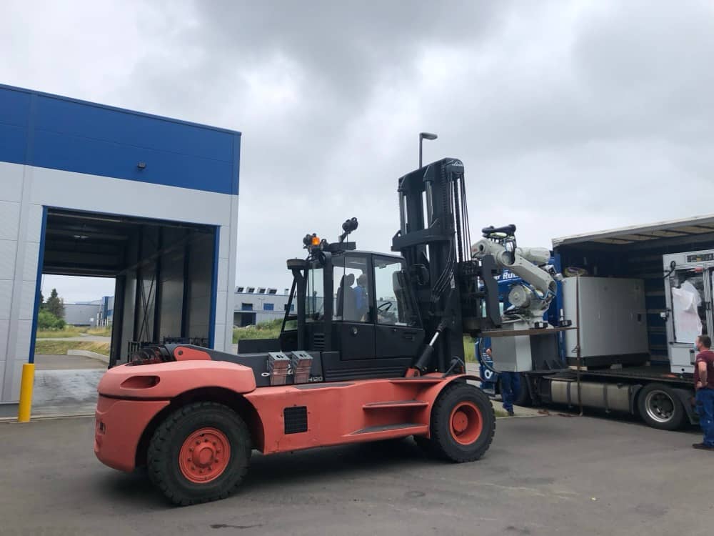 Vykládka těžkého stroje z kamionu pomocí velkého vozíku.