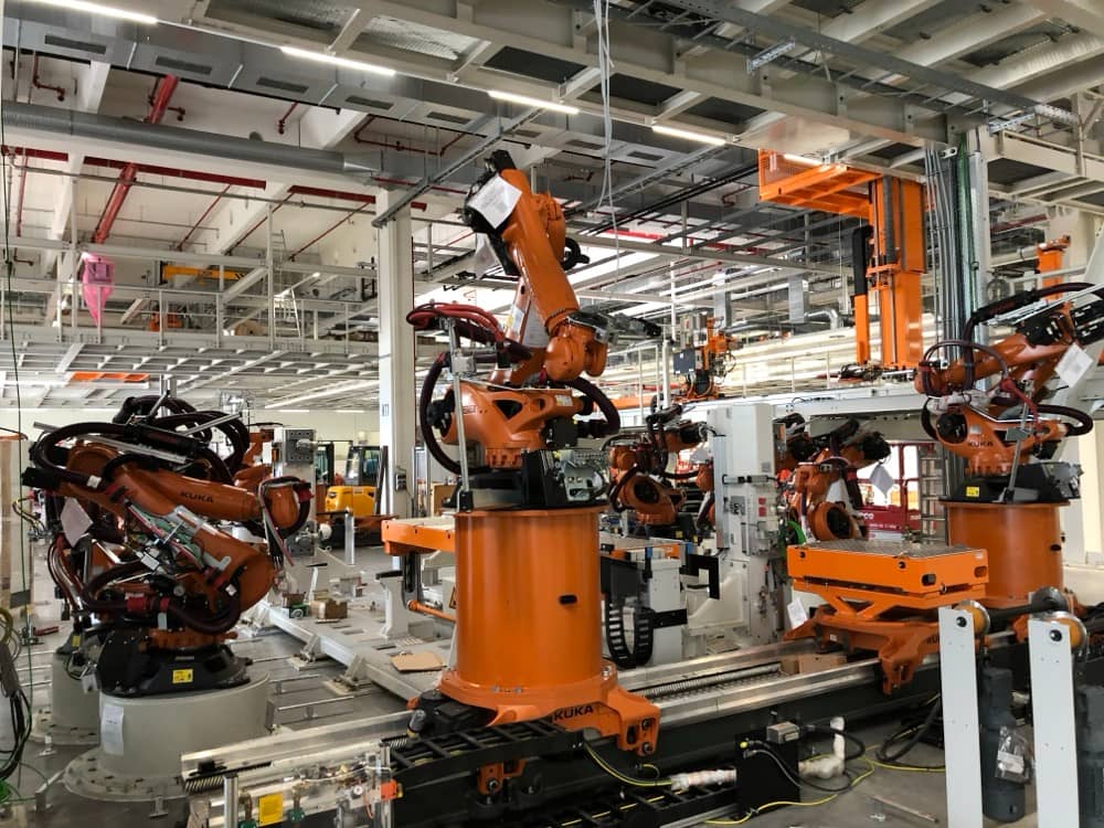 Průmyslová hala se skupinou oranžových robotů KUKA.